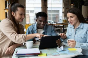 A trio of young people gathered around a table, focused on a tablet, discussing and exchanging thoughts.